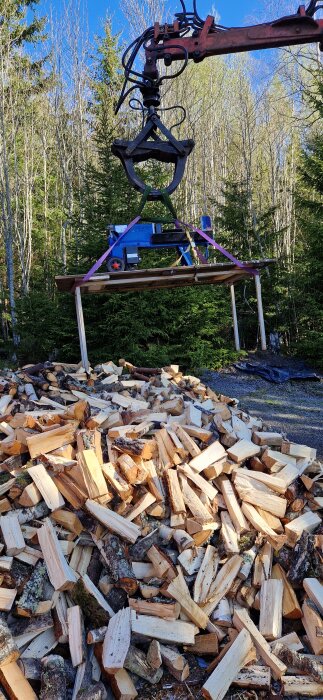 Grip lyfter en klyv över en hög med vedklabbar ute i skogen.