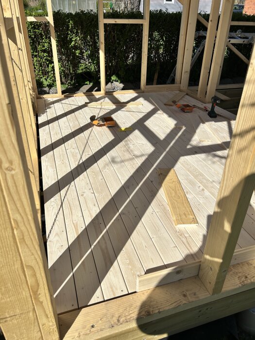 Byggstruktur av trä med nylagt bastugolv och skugga av reglar. Skruvdragare och skruvförpackningar ligger på golvet.