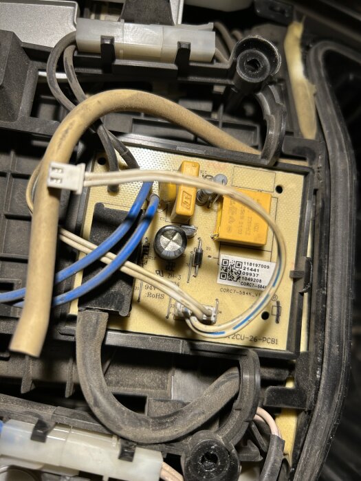Kretskort med kablar och komponenter, inklusive en synlig kondensator, inuti en elektronisk enhet.