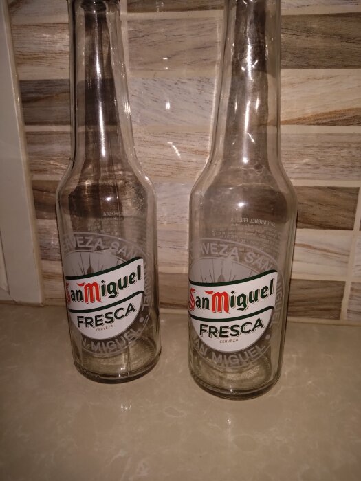 Två tomma San Miguel Fresca-flaskor på ett köksbänk, mot en bakgrund av kaklade väggar.