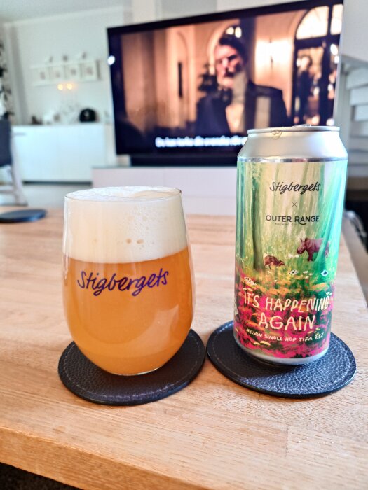 En burk Stigbergets öl med texten "It's Happening Again" och ett glas öl på ett bord, TV i bakgrunden.