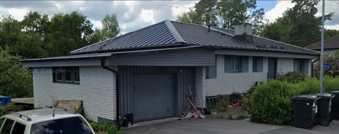 Garage med nytt lutande plåttak, ersätter tidigare platt papptak från 70-talet. Omgiven av träd, bil parkerad framför.