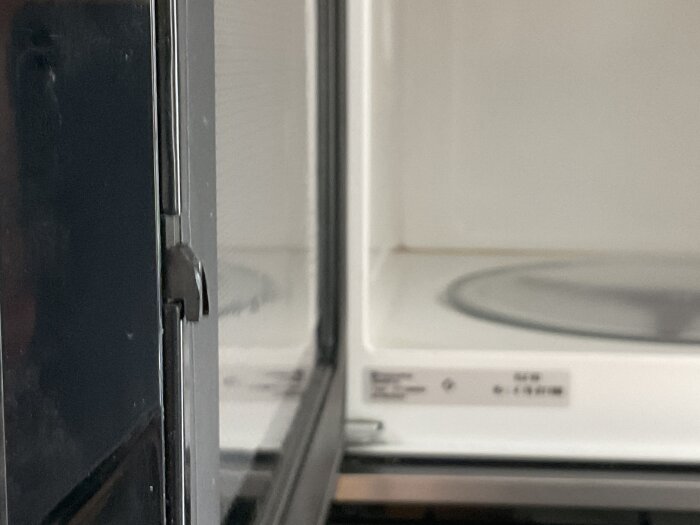 Närbild av låskroken på en gammal Husqvarna mikrovågsugn, dörren är delvis öppen.