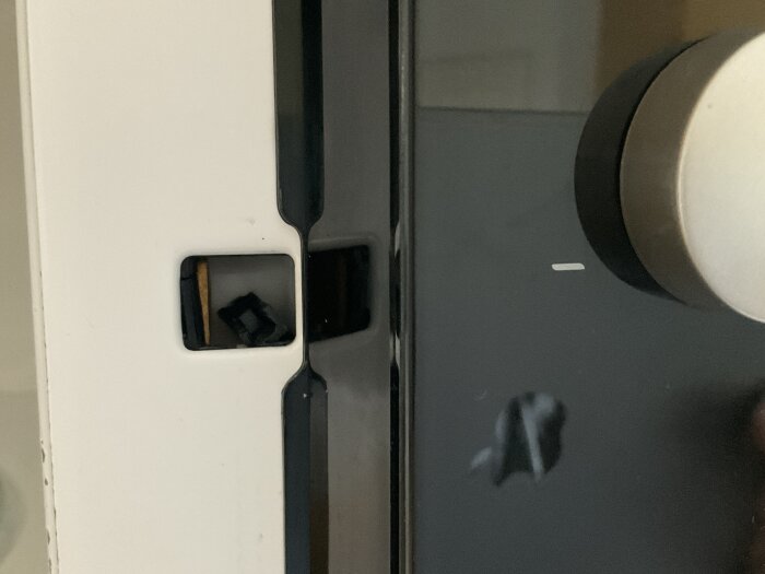 Låskrok till en gammal Husqvarna mikrovågsugn, delvis synlig och trasig, häftad mellan vit och svart plast.