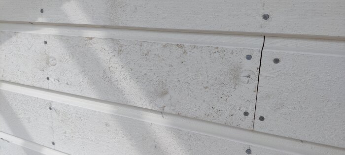 Närbild av grundmålad träfasad med spår av lera och borstningseffekter.