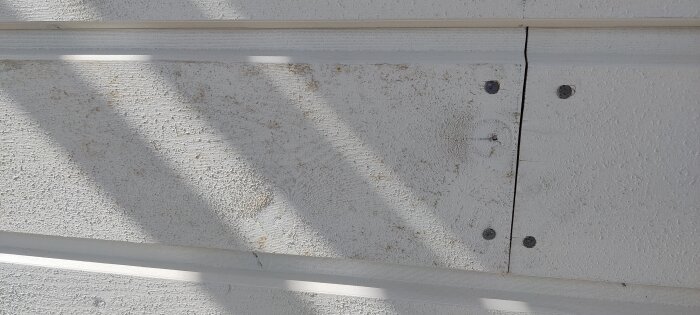 Grundmålad fasad med smutsfläckar, visar brädor före och efter borstning för att avlägsna märken från leriga skor.