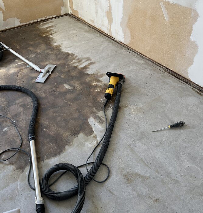 Giraffslip och verktyg på betonggolv under borttagning av matta och limrester.