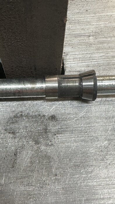 Metallhylsa monterad på en axel som ligger mot ett slipverktyg, med fokus på modifiering av hylsans omkrets och problem med monteringen.