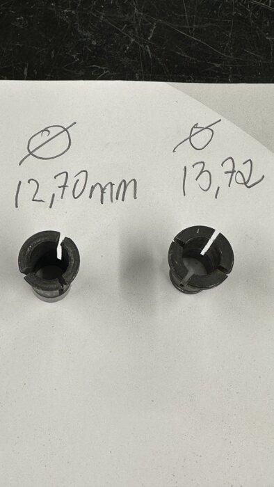 Två hylsor med måtten 12,70 mm och 13,72 mm sitter på en vit yta, märkte för bearbetning eller justering.