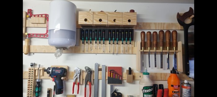 Verktygstavla med skruvmejslar, tänger, borrmaskin och handverktyg prydligt organiserade på väggen.
