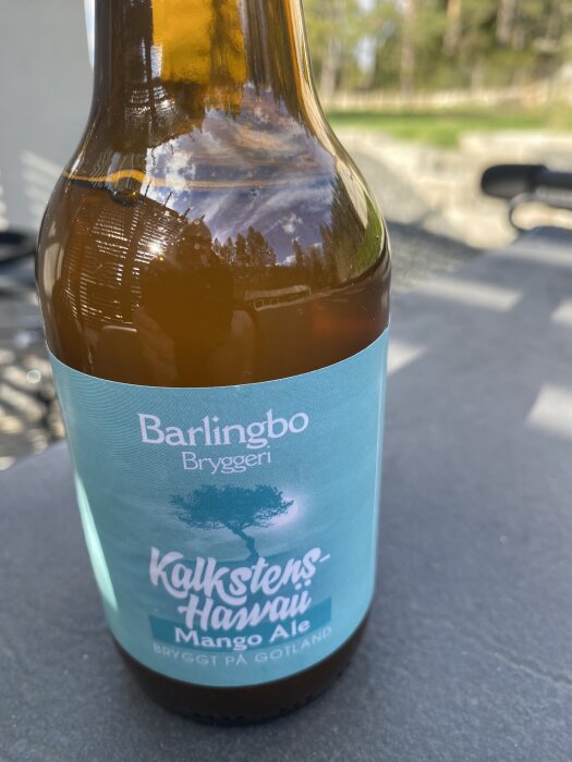 Flaska med Barlingbo Bryggeri Kalkstens-Hawaii Mango Ale, fotograferad utomhus på ett bord i solljuset.