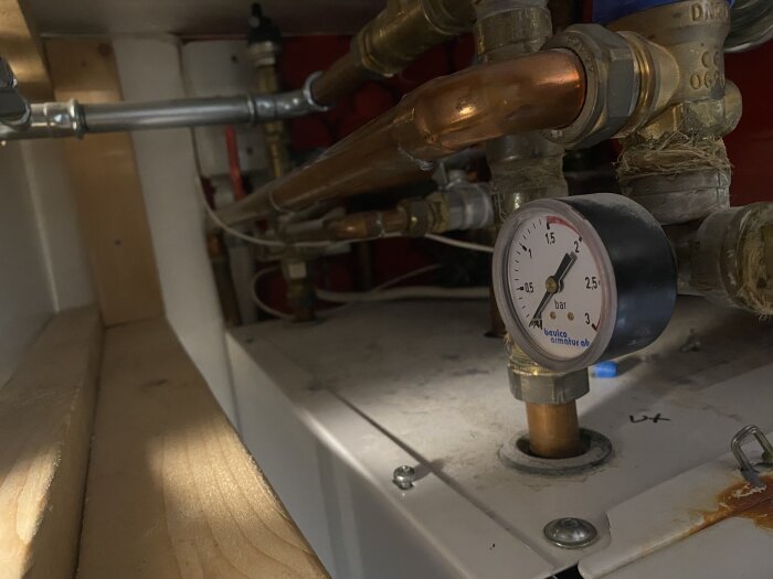 Manometer på bergvärmepump visar tryck nära 0 bar istället för vanliga 0.8, omgiven av kopparrör och ventiler.