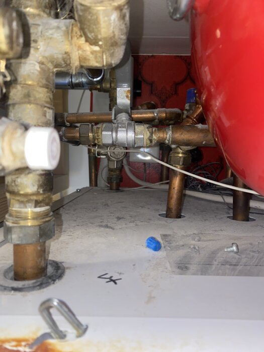 Bilden visar rörkopplingar och ventiler i ett bergvärmesystem, med fokusering på rör och anslutningar, omgiven av en röd trycktank.