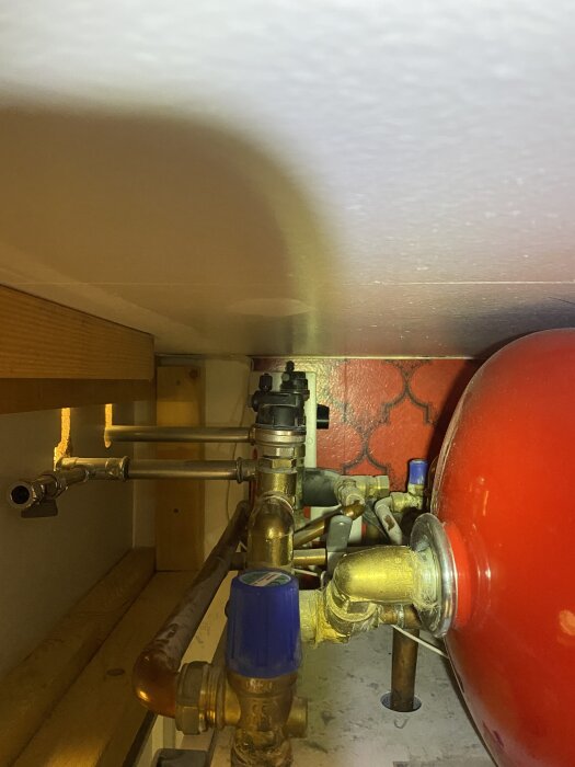 Bilden visar bergvärmesystemets rör och ventiler, med ett rött expansionskärl, i en hörna av ett teknikutrymme.