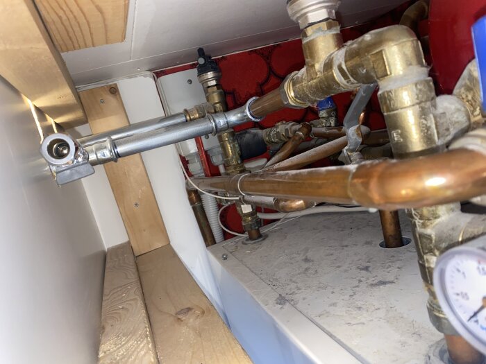 Rörledningar och ventiler i ett bergvärmesystem med synliga kopparrör och en tryckmätare, sannolikt under ett uppvärmningssystem.