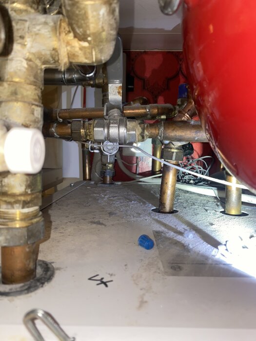 Rör och ventil till bergvärmepump underhållssystem, med ett rött tryckkärl och en blå skyddskåpa synlig på en dammig yta.