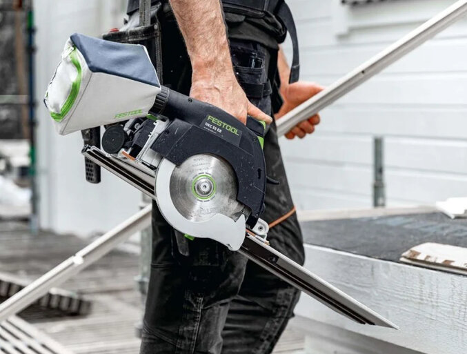 Festool cirkelsåg HKC 55 med skena, hålls av en person vid ett byggprojekt.