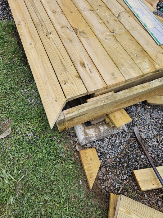 Byggprojekt pågår med en delvis färdig trall och löst placerade brädor ovanpå, synlig mark och verktyg vid kanten av altanen.