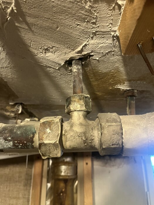 T-koppling i ett tak med kopparrör anslutna, omgiven av sliten puts och träbjälkar.
