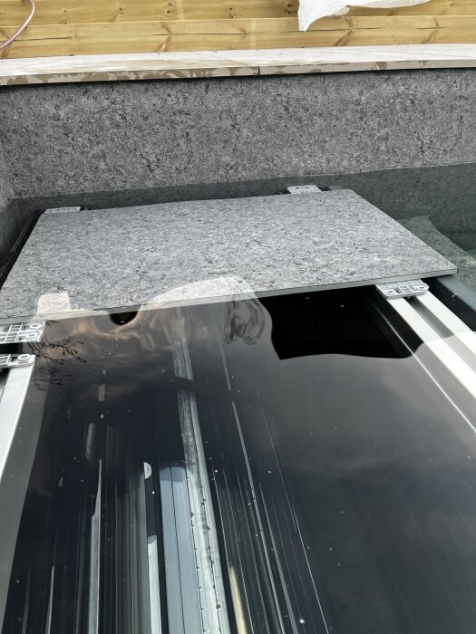 Grå stenskiva placerad på ett oavslutat bygge, med en trävägg i bakgrunden. Skivan används för att testa passformen på konstruktionen.