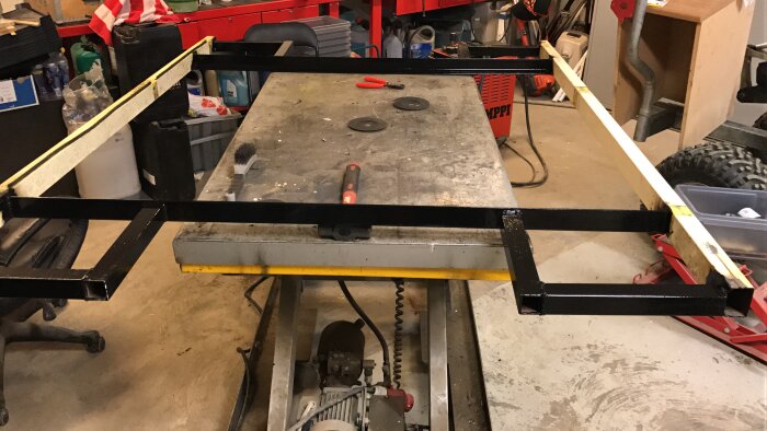 Lyftbord med breddning för ATVer i ett garage, med verktyg och material runtomkring.