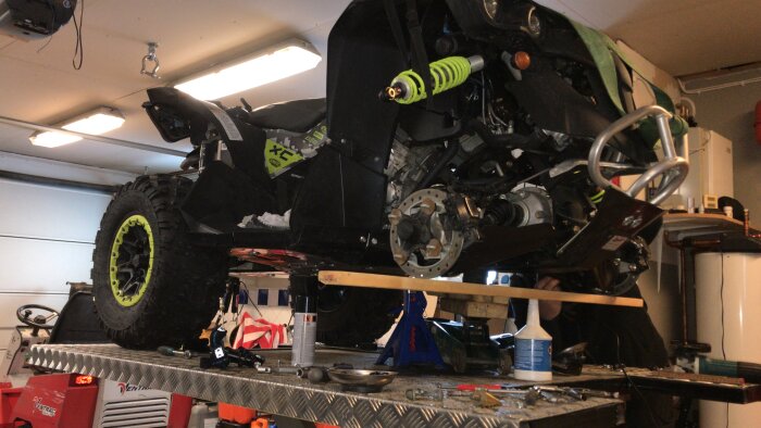Lyftbord med ATV under ombyggnad i ett garage, visar verktyg och komponenter runt omkring för reparation eller justering.