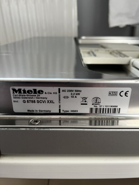 Etikett på Miele G 5786 SCVi XXL diskmaskin med specifikationer som AC 230V, 50Hz och tillverkningsdetaljer, fotograferad i ett köksutrymme.