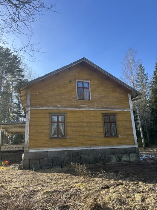Gult timmerhus från 1890 på rektangulära stenblock, med torpargrund, diskuteras för potentiell renovering av grund och dränering.