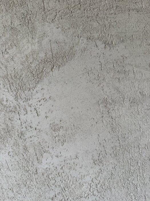 Oslipad gipsad väggyta med ojämn skrovlig struktur och små områden av slätare finish.