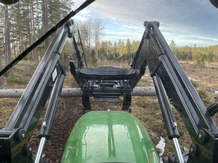 Traktor med timmergrip flyttar en stor stock i skogsmiljö.