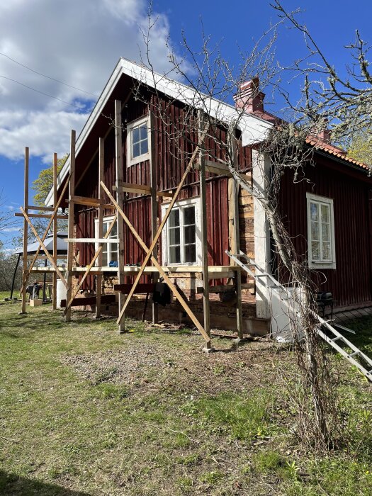 Renovering av rött hus med exponerade stockar och stödbrädor, fönsterbyte på gång, klart väder.