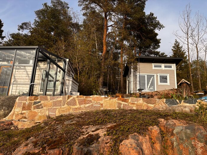 Altan med stenmur och två byggnader i skogsmiljö, den ena med stora glasfönster. Terrängen är bergig och delvis lutande.