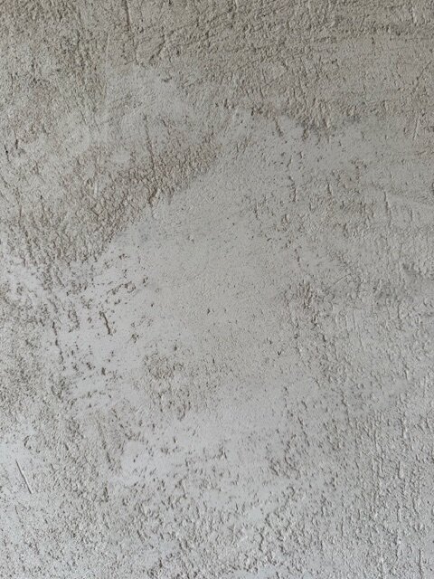 Grov och ojämn gipsputsad vägg med synliga mönster och ojämnheter som söks jämnas ut för ett sidenmatt utseende utan målning.