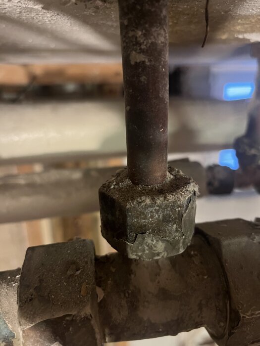 Rostigt metallrör med mutter i närbild, del av VVS-installation, gammal och sliten med korrosion, i behov av åtgärd.