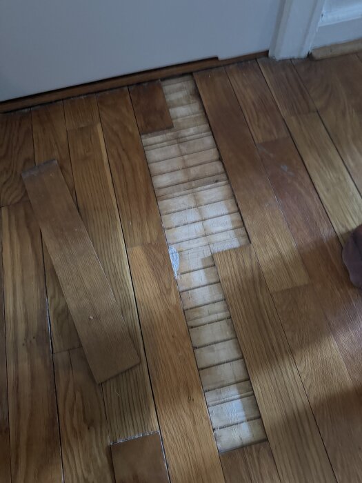 Närbild av ett trägolv med lösa parkettstavar och en del av skivan under golvet synlig.