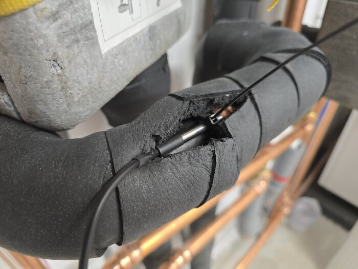 Temperaturgivare installerad på ett isolerat rör i ett kylsystem, fastsatt med buntband och delvis omsluten av svart armaflex-isolering.