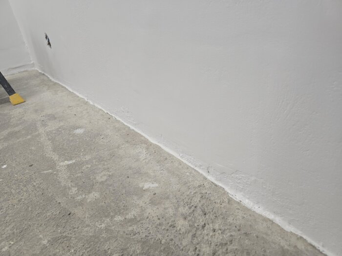 Golvet längs väggen har en tätad glipa mellan betong och vägg för att förhindra att insekter kryper in, inför plattsättning.
