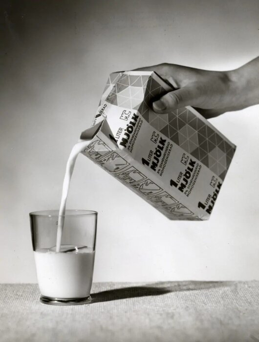 En person häller mjölk från en Tetra-förpackning i ett glas.