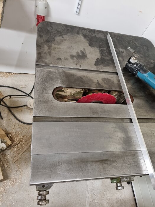 Bord med metallskiva slipad med sandpapper, slipmaskin och en röd sågklinga under spåret. Verktyg och sågspån runt om.