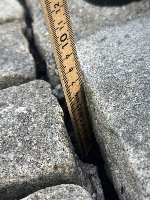 Mätdon visar djupet på breda fogar mellan gatstenar, cirka 6–7 cm djupt. Stenarna är nyligen rengjorda från mossa och gräs med högtryckstvätt.
