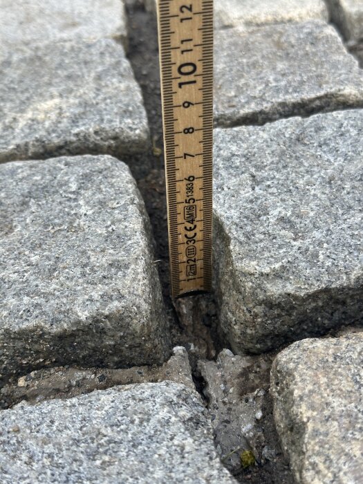 Linjal som mäter djupet på en bred fog mellan gatstenar, cirka 7 cm.