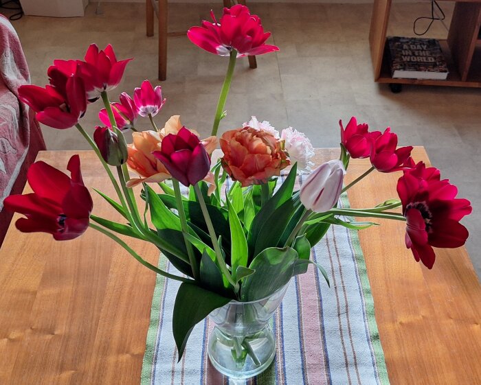 En vas med utslagna röda tulpaner står på ett bord med en randig bordslöpare.
