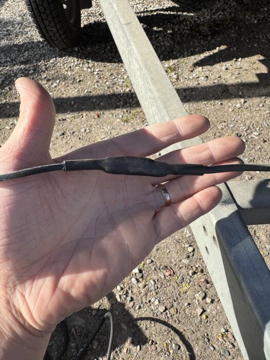 Krympslang över skarvat kabel i hand, utomhusmiljö.