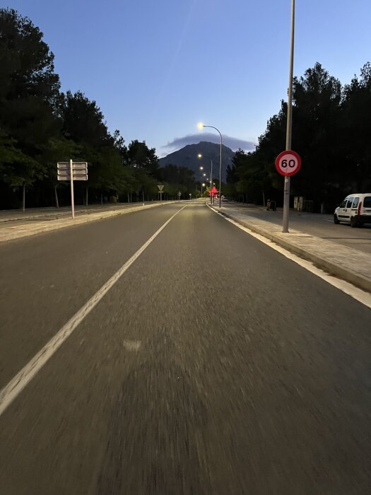 Tidig morgon eller sen kväll på en stadsgata, med ett hastighetsbegränsningsskylt på 60 km/h, gatlyktor och en skymt av ett berg i bakgrunden.