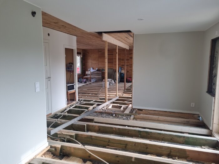 Renovering pågår med öppnade golvbjälklag och borttagen kutterspån. Rum med blottade väggar och dörröppningar, förberett för nya balkar.