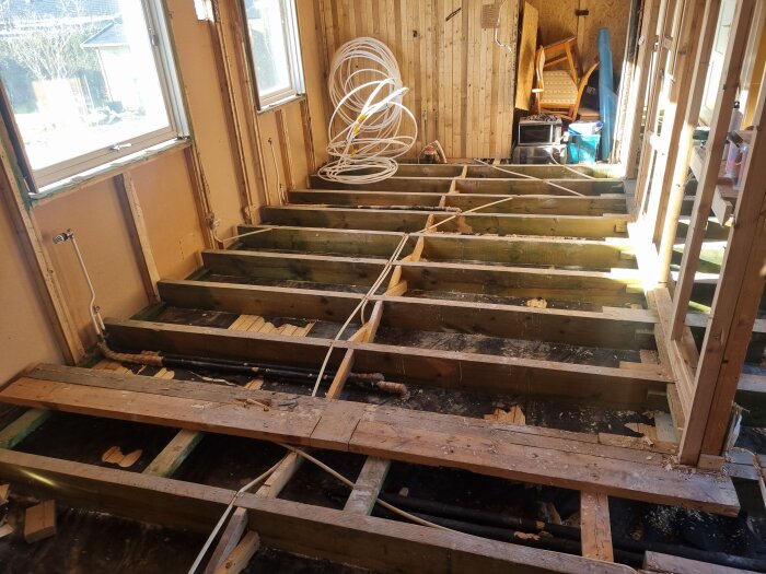 Inre rum under renovering med frilagda bjälkar, borttagna golvplankor och installation av nya balkar. Fönster byta ut för bättre stöd.