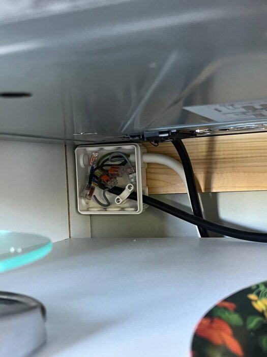 Öppen kopplingsdosa med synliga kablar under köksbänk vid diskmaskin.