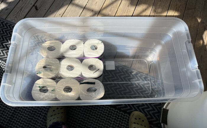 Plastlåda med nio plastförpackningar av toapapper i två rader på golvet.