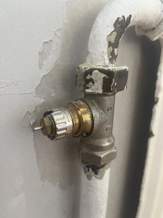 Radiatorventil med en metallisk ställskruv istället för en termostat, monterad nära en vägg med rör och flagnande färg.