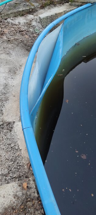 Skadad poolkant med blå plastkant och vattenskadad liner; poolväggen har lossnat och lyft ojämnt, vilket gör linern bucklig.